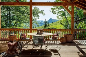Een houten terras met een ronde tafel en stoelen, met uitzicht op een bergachtig landschap.