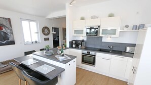 Una cucina moderna con mobili bianchi, un'isola centrale e un'area pranzo con sedie.
