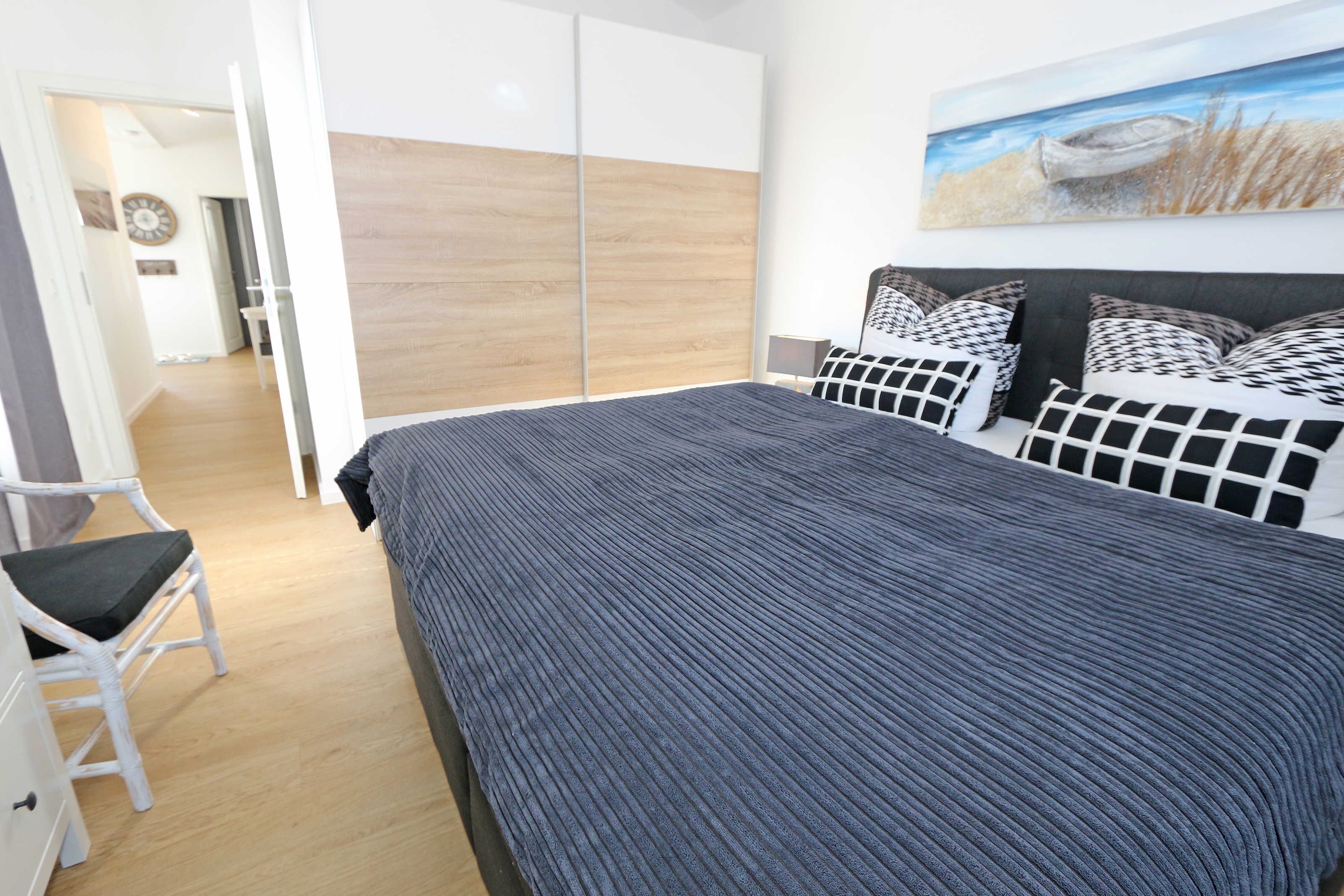 Ein Schlafzimmer mit einem großen Bett, einem Kleiderschrank, einem Sessel und einem Bild an der Wand.