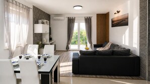 Een moderne woonkamer met een eethoek, een bank, een televisie en een balkon met gordijnen.