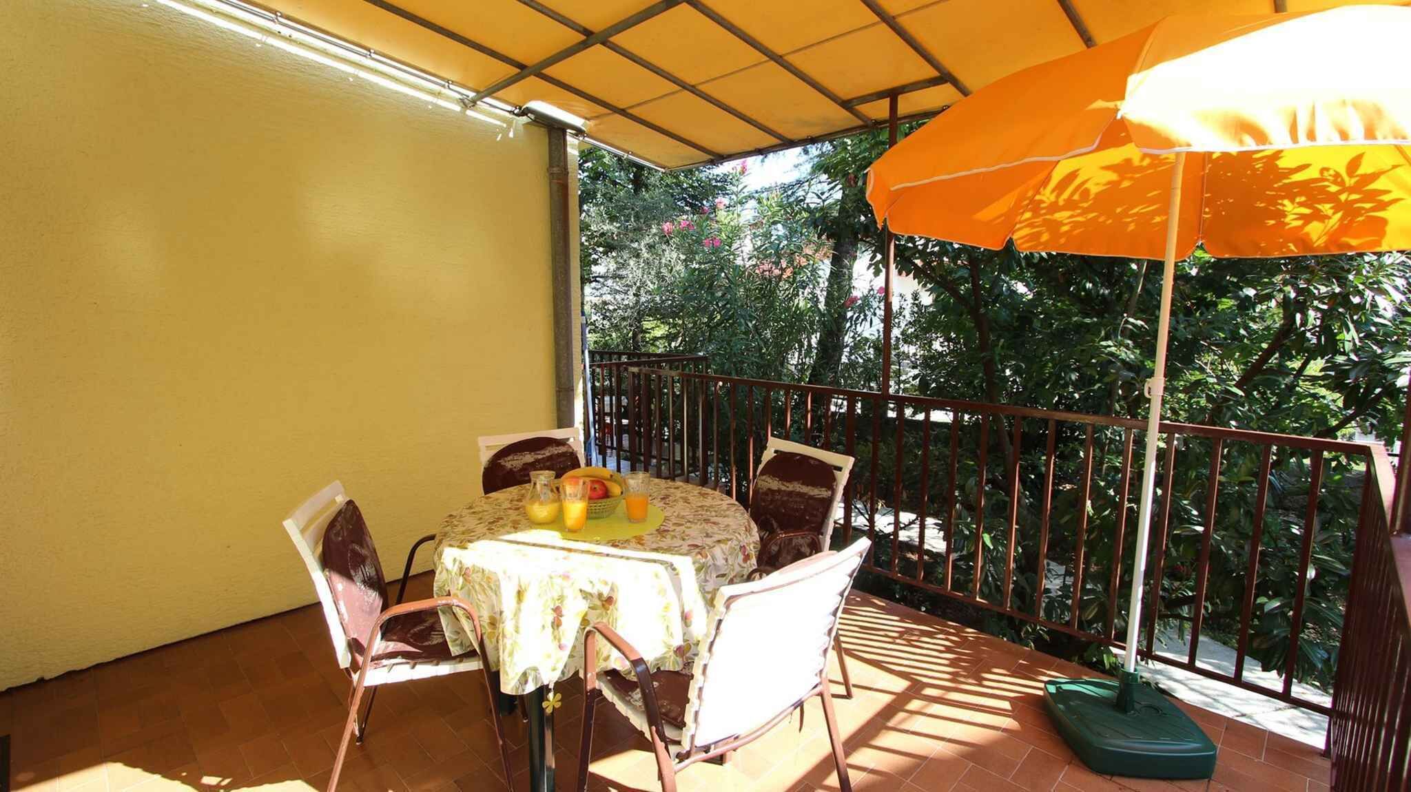 A covered outdoor patio with a table and chairs, surrounded by a metal railing and greenery.