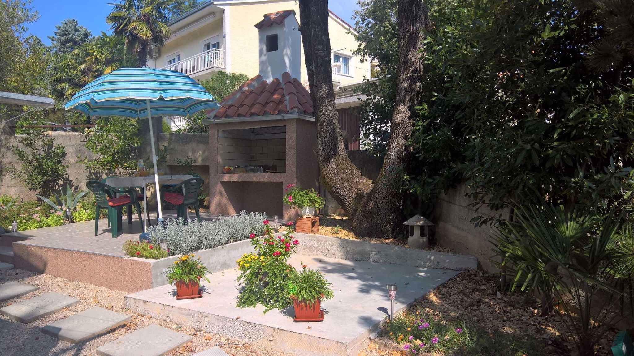 An outdoor patio with a table and chairs, a blue umbrella, and potted plants.