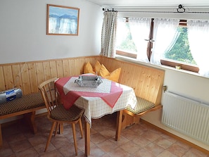 A corner dining area with a table set for two, wooden chairs, a radio, and a window with curtains.