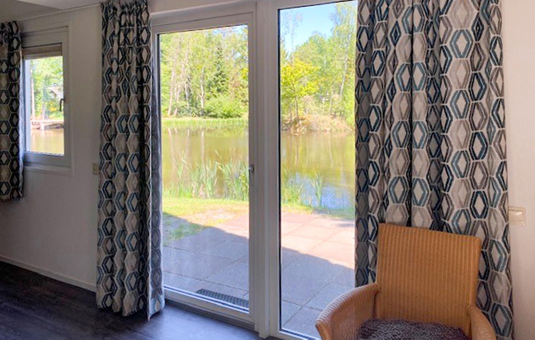 A room with a large sliding glass door leading to a patio with a view of a lake and trees.