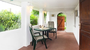 Une terrasse couverte avec une table et des chaises, une porte en bois et une vue sur la verdure.