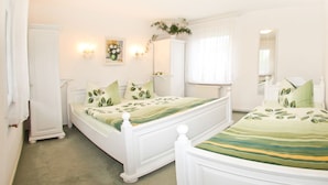 Une chambre à coucher avec deux lits blancs, une armoire blanche, un miroir et un luminaire fixé au mur.