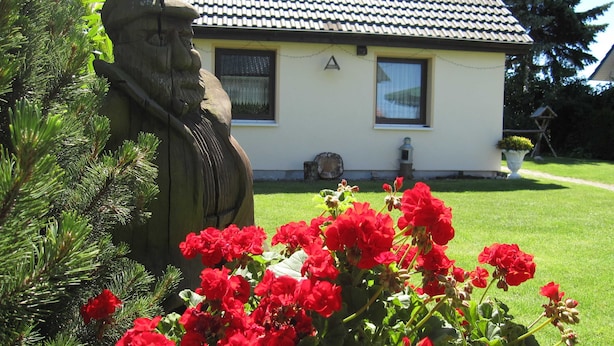 Une maison avec un toit en tuiles, une statue et des fleurs rouges au premier plan.