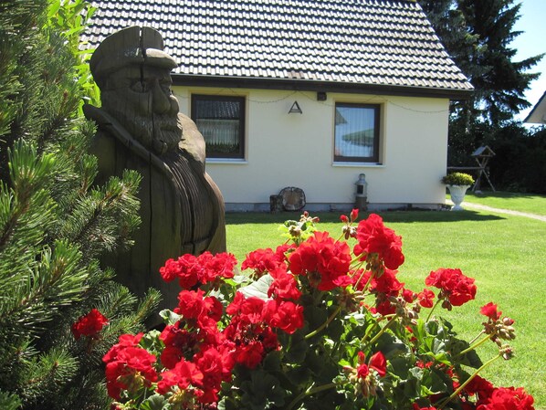 Une maison avec un toit en tuiles, une statue et des fleurs rouges au premier plan.