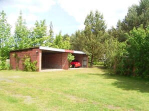 Un petit bâtiment en briques avec un garage, entouré d’arbres et d’herbe.