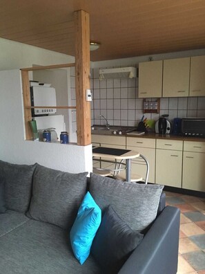 A modern kitchen with a dining area, a sofa with cushions, and a tiled floor.