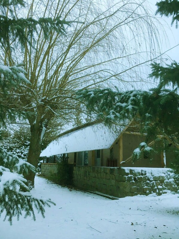 A stone building with a snow-covered roof, surrounded by trees.