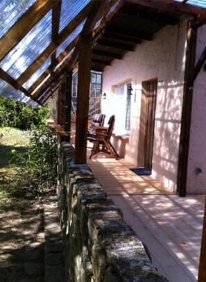 Un patio cubierto con paredes de piedra, suelo de madera y una mesa con sillas.