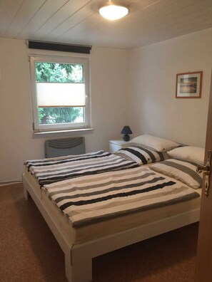 A bedroom with a bed, a window, a radiator, a lamp, and a framed picture on the wall.