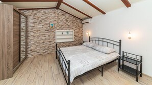 A bedroom with a stone wall, a bed with a metal frame, a wooden floor, and a sloped ceiling with wooden beams.