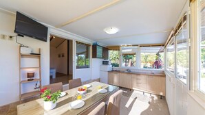 A modern kitchen with a dining area, a TV mounted on the wall, and a view of the outdoors.