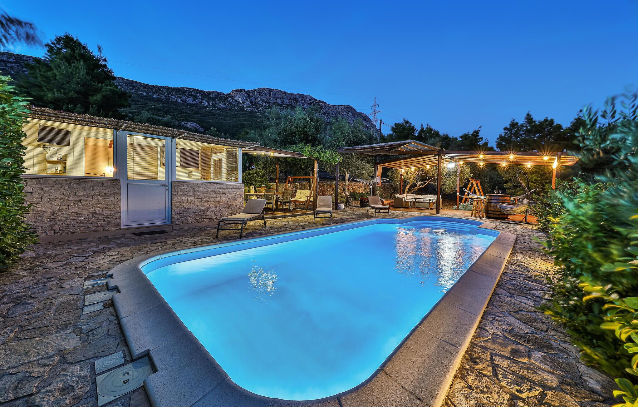 A swimming pool with a stone deck, surrounded by outdoor furniture and a covered seating area.