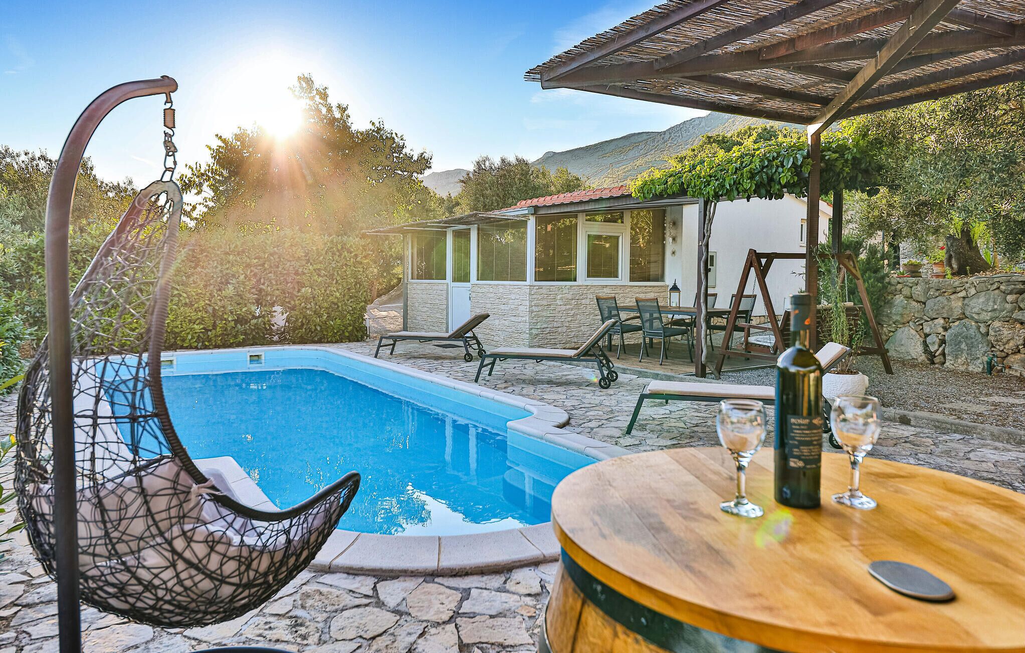 A pool area with a hanging chair, a table with glasses, and a pergola.