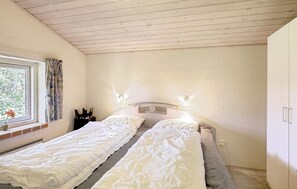 Ein Schlafzimmer mit zwei Einzelbetten, einem Fenster mit Vorhängen, einem Nachttisch mit Schneidebrett und einem Kleiderschrank.