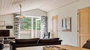 En moderne stue med træloft, sofa, et bord med et brætspil, fjernsyn og en dør.