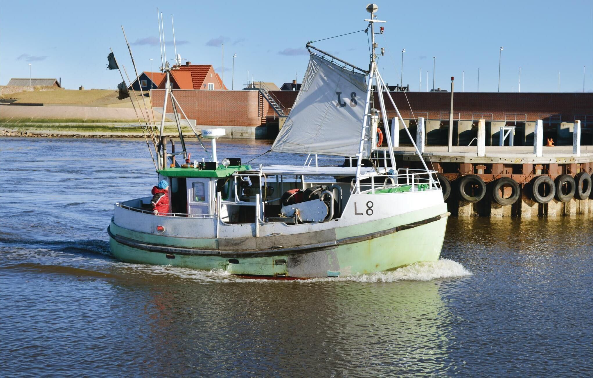 A small fishing boat with the number L8 on its side, docked at a pier with a row of tires.
