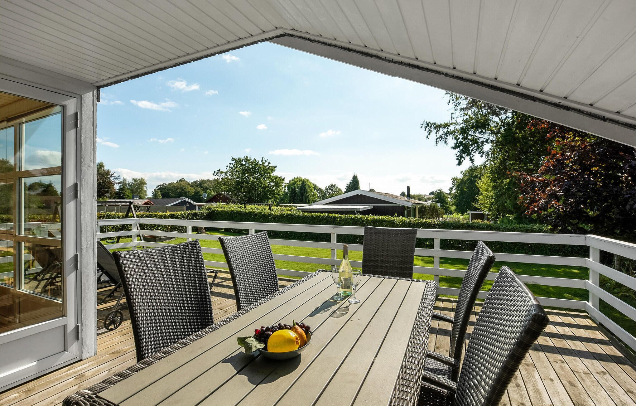 Eine Terrasse im Freien mit Korbmöbeln und einem Tisch für zwei Personen, mit Blick auf eine grüne Landschaft mit Häusern.