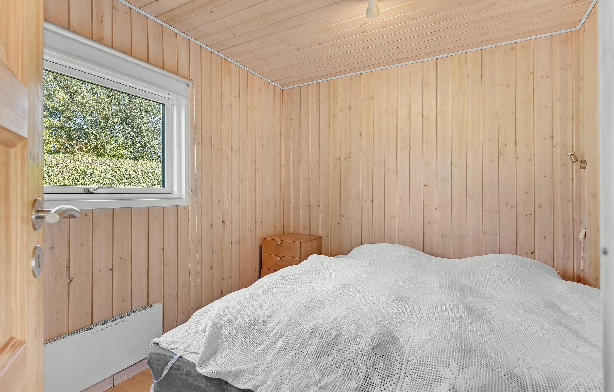A wooden-paneled room with a bed, a window, and a radiator.