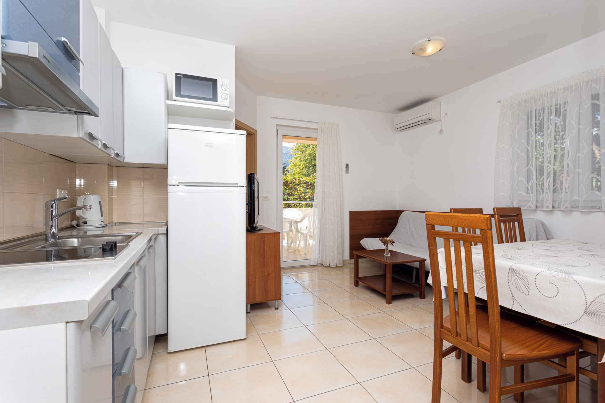 A compact kitchen with a refrigerator, microwave, and sink. There is a dining area with a table and chairs, and a small seating area with a sofa.