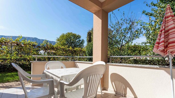 A patio with a table and chairs, a striped umbrella, and a view of trees and mountains. - Holiday apartment only 100 m from the sea (Baška)