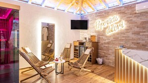 Ein gemütlicher Lounge-Bereich mit Holzliegen, einem kleinen runden Tisch und einer Ziegelwand mit leuchtendem Neonzeichen.