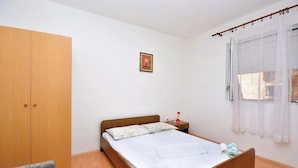Une chambre avec un lit en bois, une petite table de chevet, une chaise, une armoire, une fenêtre avec des rideaux et un tableau accroché au mur.