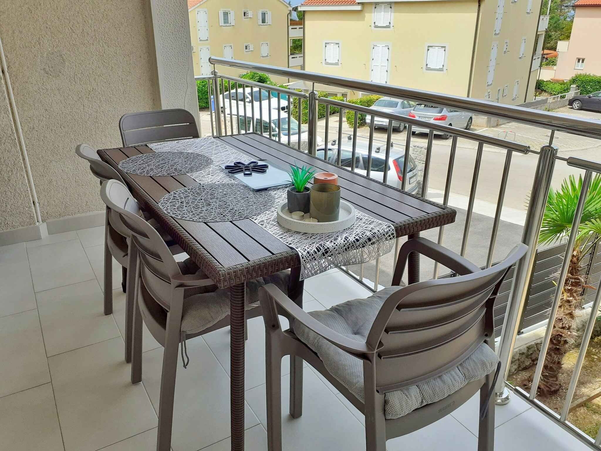 Un balcon avec une table et des chaises, un pot de fleurs et une vue sur la rue.