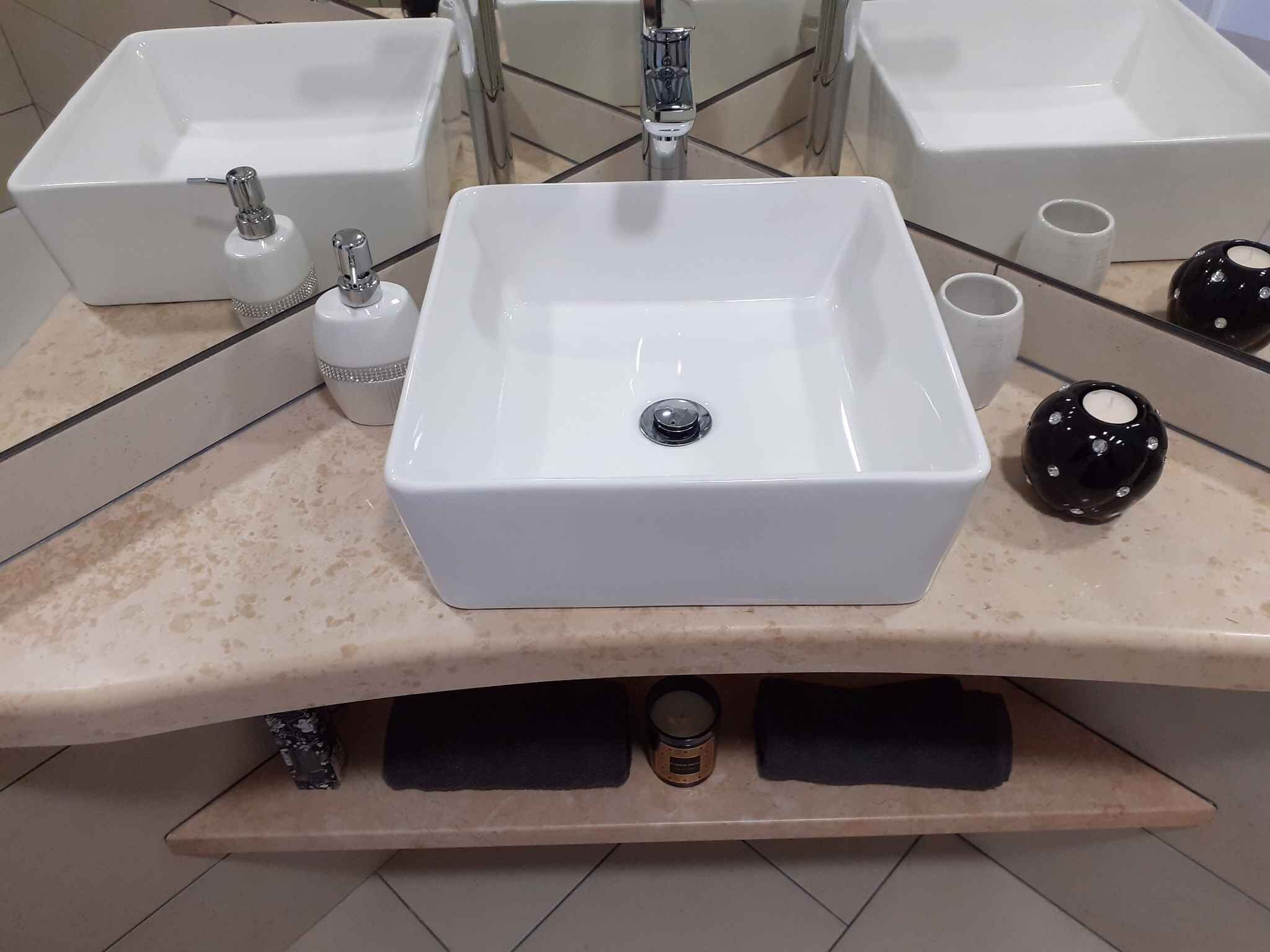 A bathroom with a central white sink, two faucets, a mirror, and a black decorative object.