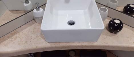A bathroom with a central white sink, two faucets, a mirror, and a black decorative object.
