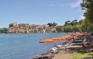 A waterfront promenade with rows of sun loungers and orange umbrellas, a backdrop of historic buildings, and a clear blue sky. - Amazing home in Anguillara Sabazia RM (Anguillara Sabazia RM)