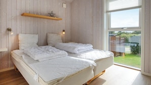 Un dormitorio con dos camas, paredes de madera, una ventana con vistas a la vegetación y una estantería con un objeto en forma de estrella.