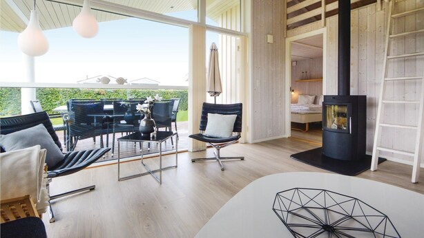 Una habitación amplia con un ventanal grande, una chimenea moderna y una zona de comedor con sillas y una mesa.