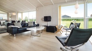 Una sala de estar moderna con un sofá de cuero negro, una mesa de centro redonda y un amplio ventanal con vistas al exterior.