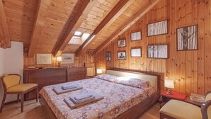 Une pièce chaleureuse, avec des murs en bois, comprenant un lit, deux chaises, un bureau et des tableaux encadrés.