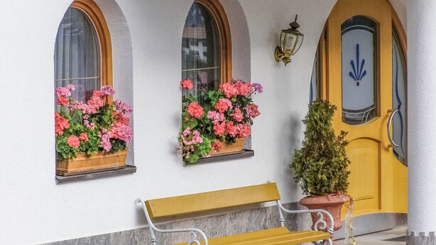 A building facade with three arched windows, a bench, a potted plant, and a door with a blue emblem. - gemuetliche Ferienwohnung (Kappl)