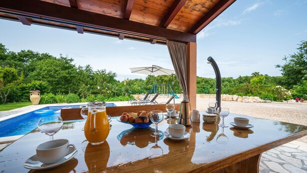 A wooden table with breakfast items and a glass of juice, overlooking a swimming pool and lush greenery. - Pet friendly home in Labin (Labin)