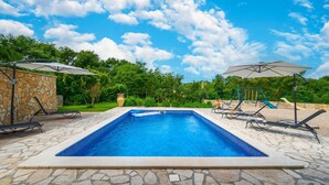 A rectangular swimming pool with a stone border, surrounded by lounge chairs and umbrellas. - Pet friendly home in Labin (Labin)