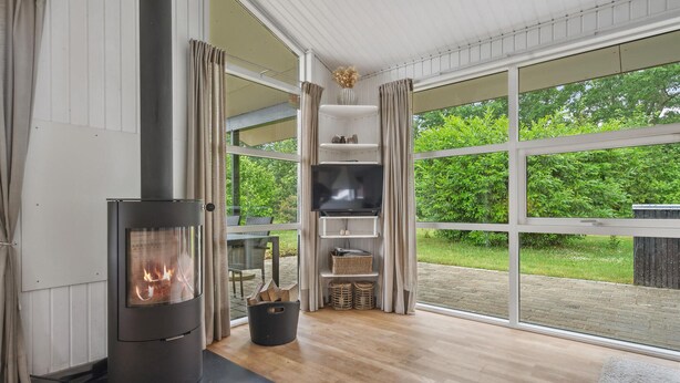 A modern living room with a wood-burning stove, a flat-screen TV, and a large window overlooking a garden.