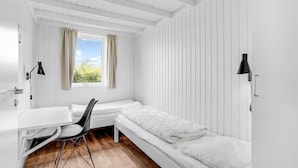 A minimalist room with a white desk, a black chair, a white bed, and a window with curtains.