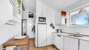 A modern kitchen with white cabinetry, a wooden countertop, a built-in microwave, a kettle, and a window with a view of trees.
