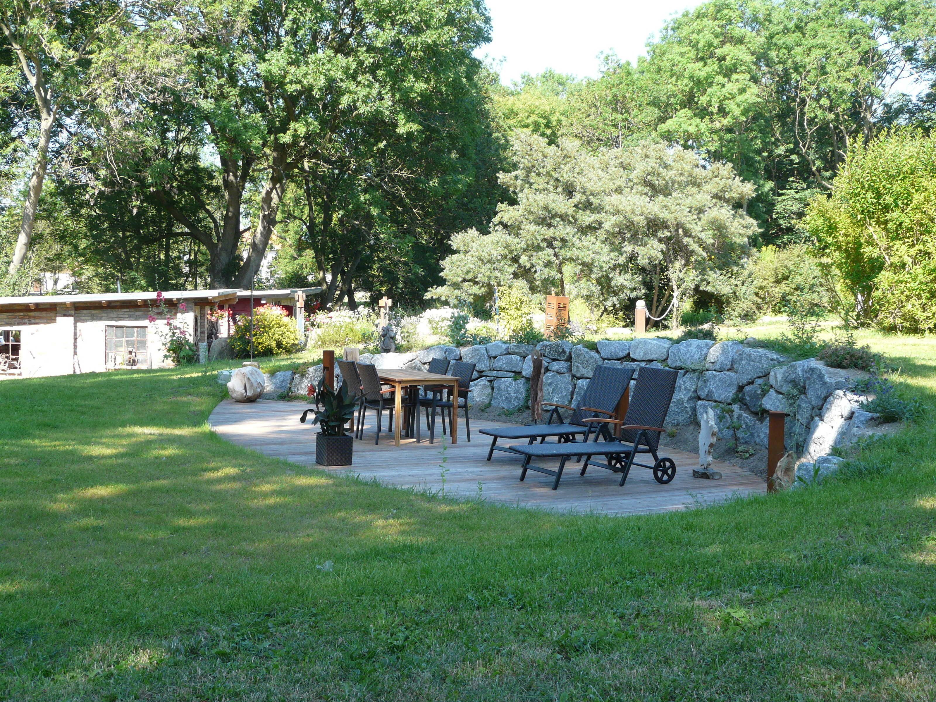 A patio with a stone wall, a wooden table, and chairs.