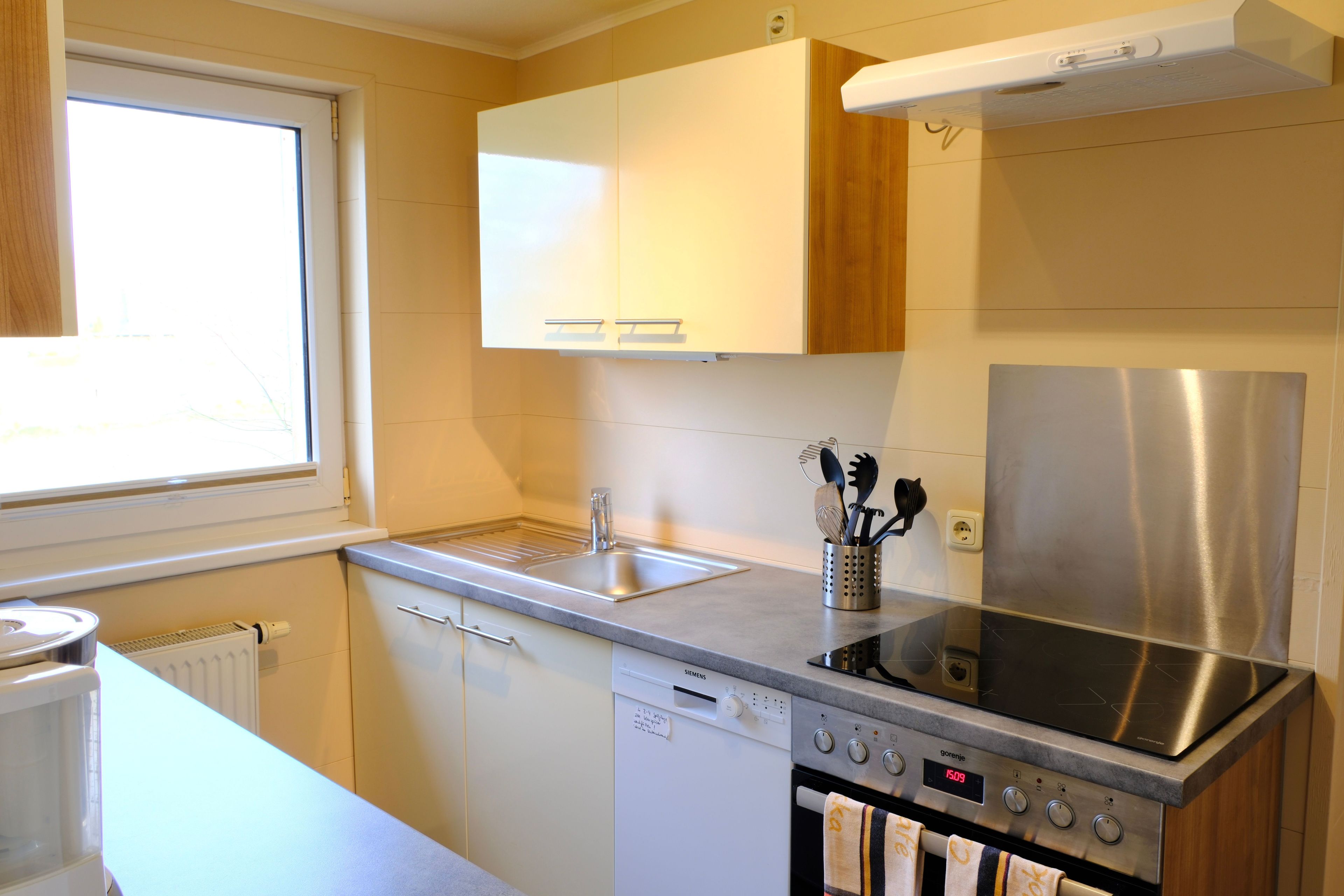 Eine moderne Küche mit Geschirrspüler, Backofen, Edelstahlkühlschrank und einem Fenster für natürliches Licht.