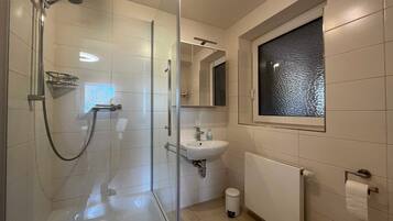 A bathroom with a glass-enclosed shower, a white sink, a mirror, and a window.