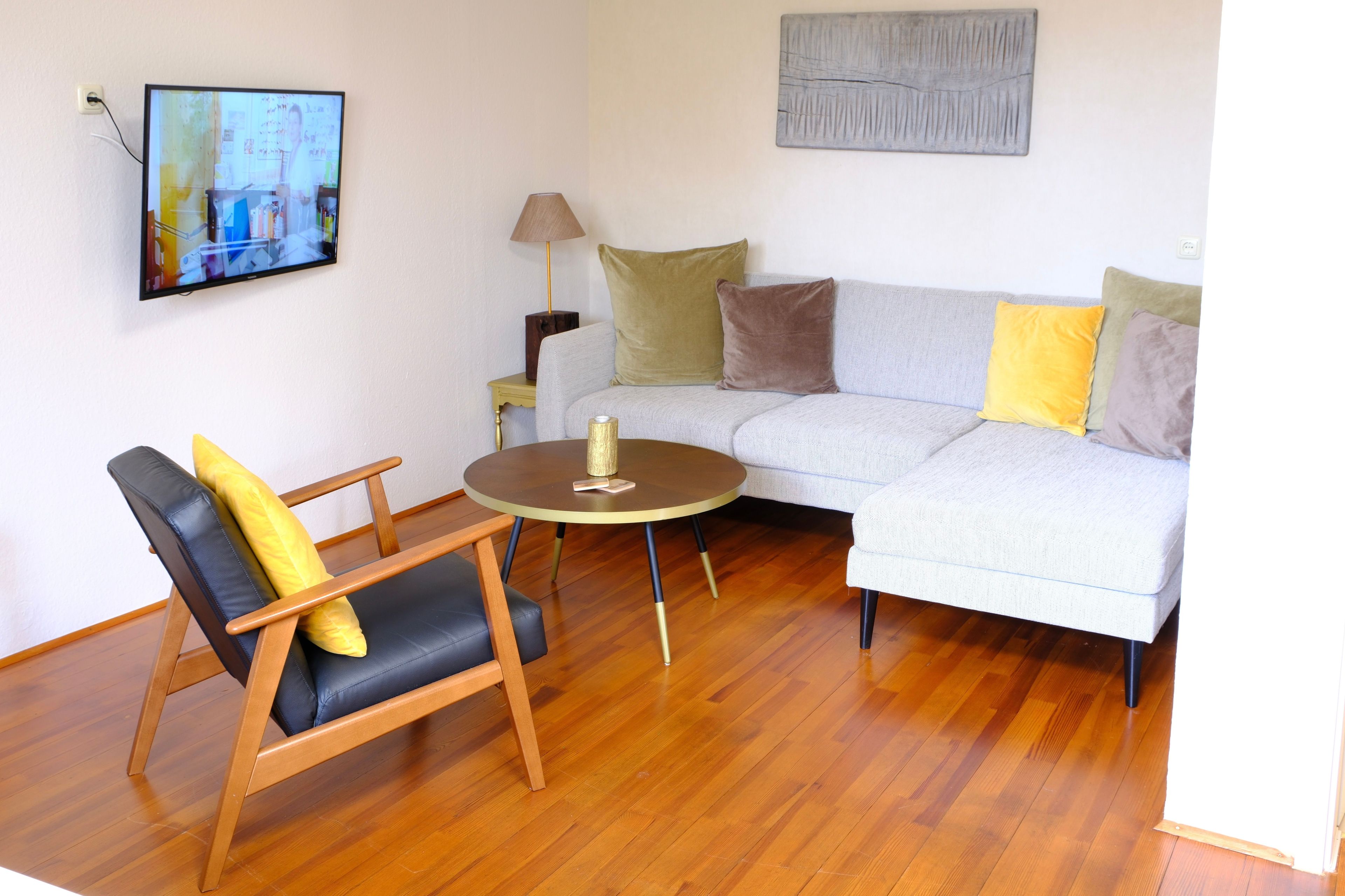 A living room with a sofa, a chair, a small table, a lamp, and a television mounted on the wall.