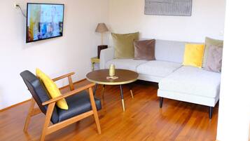 A living room with a sofa, a chair, a small table, a lamp, and a television mounted on the wall.