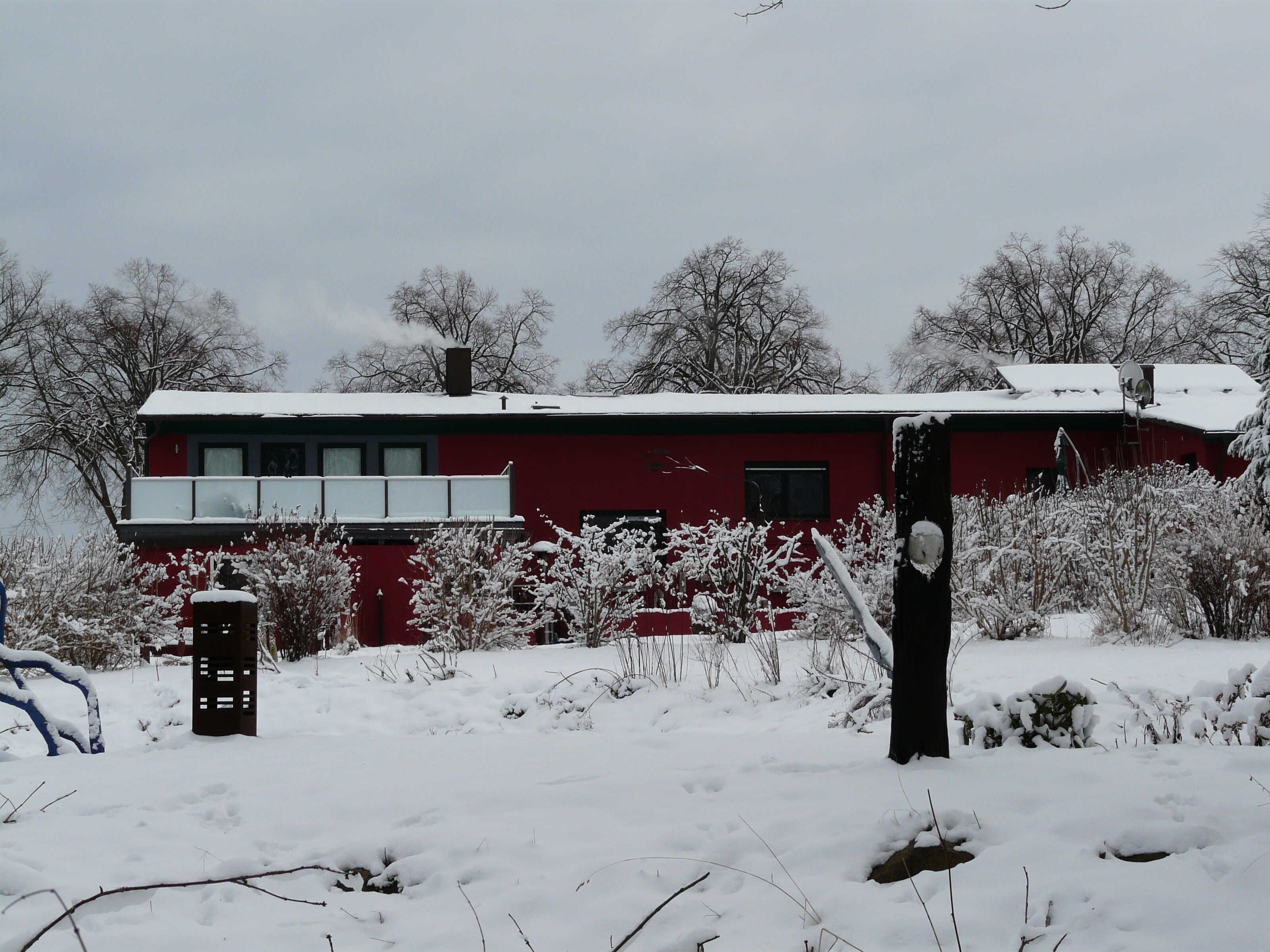 Ein rotes Gebäude mit Balkon, umgeben von schneebedeckter Vegetation.